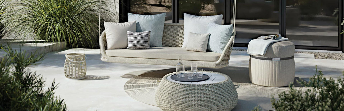 Divano e pouf da giardino in intreccio color corda su una terrazza, con tavolino basso e piante