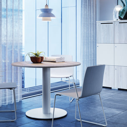 Tavolo tondo Frezza alto 74 cm con due sedie in un'area lounge accanto alla vetrata