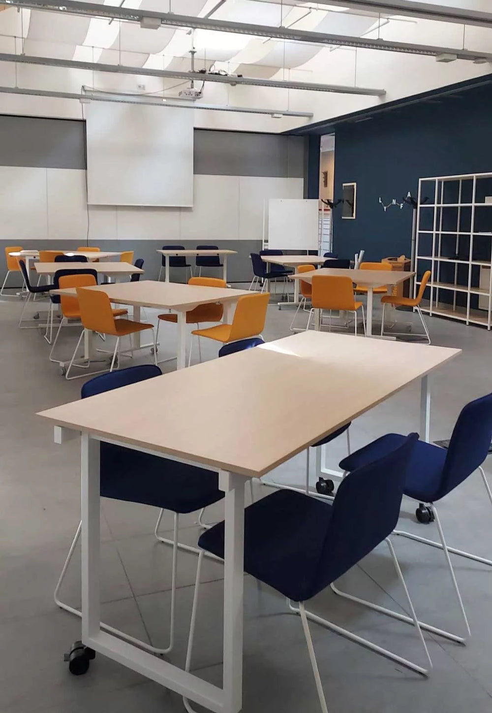 Sala arredata con tavoli su ruote, sedute a slitta e librerie a giorno, realizzata da Isoardi Group