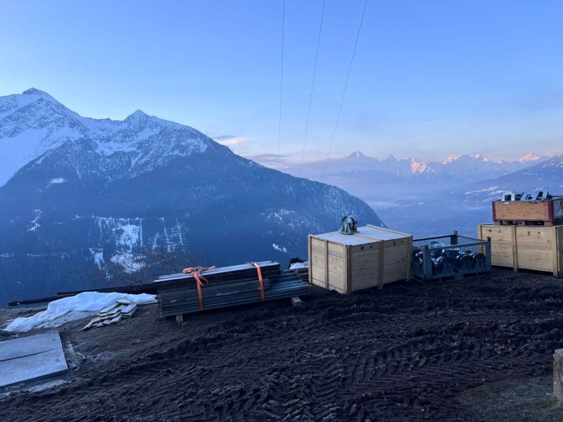 Cantiere in quota per il box di controllo di un impianto idroelettrico, con casse di materiale e montagne sullo sfondo