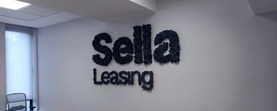 Logotipo aziendale Sella Leasing in lichene stabilizzato scuro su parete bianca